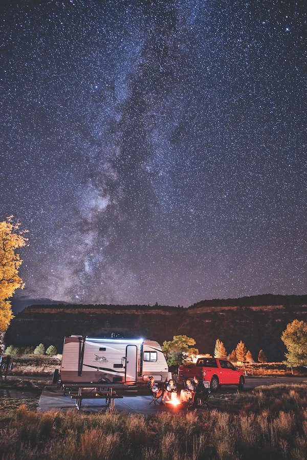 A Jayco RV camping family sits around a campfire at night under the milky way